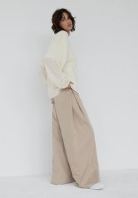 Kremowy, oversize'owy sweter z opuszczonymi ramionami w połączeniu z beżowymi szerokimi spodniami z bocznymi kieszeniami i tylnymi kieszeniami typu welt.