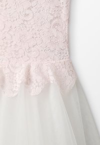 Lichtroze kanten lijfje met florale patronen, gegolfde zoom en gelaagde witte tule rok. Zachte textuur met een delicate, gelaagde ontwerp.