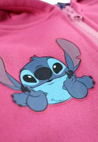 Sweatshirt en tissu rose présentant une impression colorée d'un personnage de dessin animé avec de grands yeux, des oreilles pointues et une expression malicieuse.