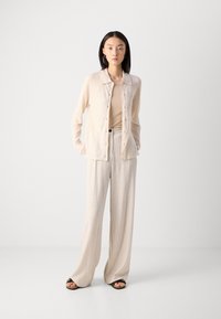 Strikket beige cardigan med knapper og krage, kombinert med stripete, vide beige bukser. Sandaler fullfører antrekket. Glatt tekstur, lett stoff.