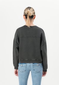 Felpa corta grigio scuro con spalle cadenti e dettagli di cucitura, abbinata a jeans attillati azzurri, vista da dietro.