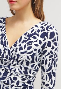 Navy and white long-sleeve dress featuring a floral pattern, v-neckline, and gathered texture at the bust for a fitted silhouette.