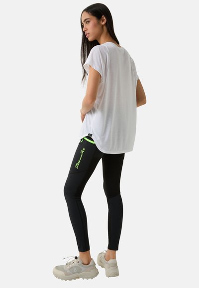 Hvid kortærmet top parret med tætsiddende sorte leggings med neonlys og logo. Lysegrå sneakers fuldender outfittet.