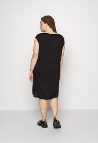 Vestido preto sem mangas feito de tecido macio, com um corte solto, cintura ajustada e pregas nas costas. Combinado com sapatos pretos.