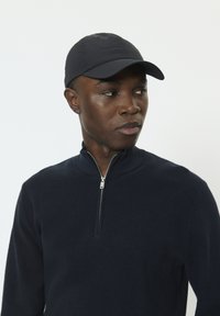 Pull en maille bleu marine avec fermeture éclair, col montant et tissu texturé, complété par une casquette assortie bleu marine. Finition lisse et coupe ajustée.