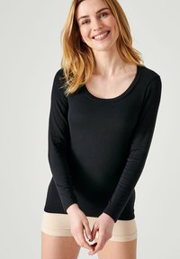 Maglietta nera a maniche lunghe con scollo tondo, realizzata in un tessuto morbido, abbinata a pantaloni corti beige chiaro, che evidenziano una silhouette aderente.