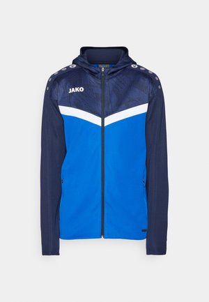 Giacca sportiva blu con zip frontale, cappuccio, sezione superiore con motivo e accenti bianchi. Presenta bottoni a pressione sulle spalle e tasche laterali.