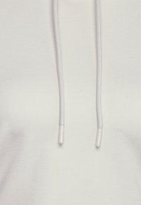 Bílá mikina s kapucí a jemnou texturou, s přední kapsou a šňůrkami v světlejší barvě. Výrazné ploché švy a minimalistický design.