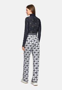 Marineblaues Spitzenoberteil mit langen Ärmeln und eng anliegendem Schnitt, kombiniert mit weißen Hosen, die ein schwarzes Grafikmuster und einen elastischen Bund haben.