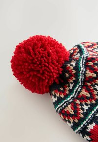 Stickad mössa med en röd pom-pom, med geometriska mönster i marinblått, rött, gräddvitt och grönt. Mjukt ullmaterial, rundad form.