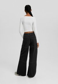Black wide-leg jeans with a relaxed fit and large back pockets. Paired with a fitted white long-sleeve top, showcasing a smooth texture.