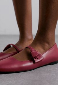 Bordo odiniai balerinų bateliai su apvaliu pirštu, dekoruoti kaspinėliu ir turintys žemą profilį. Lygi tekstūra ir minimalistiškas dizainas.