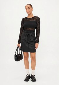 Juodas ilgomis rankovėmis megztinis su permatoma nėrinių raštu, derinamas su aptempta juoda dirbtinės odos suknele su surišama diržu ir kišenėmis. Juoda rankinė.