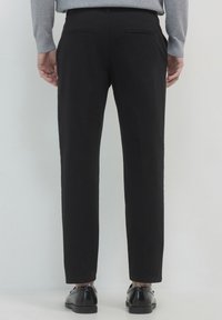 Schwarze maßgeschneiderte Hosen mit geradem Schnitt, ausgestattet mit Gesäßtaschen und einer glatten Textur, kombiniert mit schwarzen Schuhen.