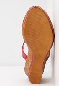 Sandale rouge avec une semelle en liège, présentant une surface texturée et un léger talon. L'intérieur a une finition lisse et des brides ajustables.
