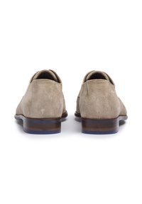 Chaussures en suède beige avec un petit talon, présentant une texture lisse et des accents contrastants en bleu et marron sur la semelle. Design à bout arrondi.