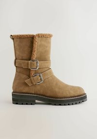 Pruuni sametist pahklesteboot, millel on kaks reguleeritavat metallist klambrit, kunstfliisi vooder ja tugev must kummitald koos tekstureeritud mustriga.