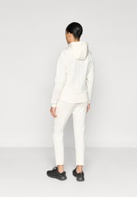 Λευκή φούτερ με κουκούλα, σε χαλαρή γραμμή, συνδυασμένη με λευκά παντελόνια jogging που ταιριάζουν. Μαύρα αθλητικά παπούτσια ολοκληρώνουν την εμφάνιση.