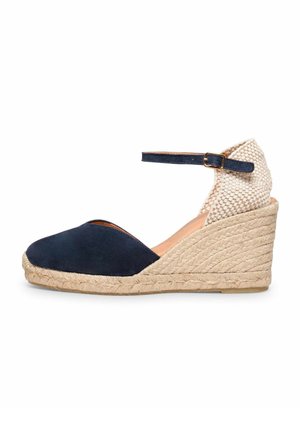 Cuña alpargata azul marino con tacón beige tejido, plataforma de yute trenzado y correa ajustable en el tobillo con hebilla dorada.