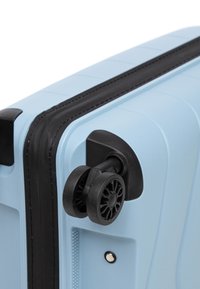 Světle modrý tvrdý kufr s texturovaným povrchem, černými akcenty a hladce se otáčejícími černými koly. Má zapuštěnou rukojeť.
