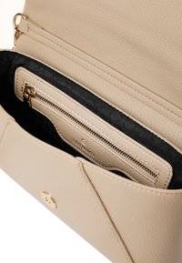 Beige læderhåndtaske med en tekstureret finish, der har en lukning med guldfarvet hardware og en inderlomme med lynlås og sort stoffor.