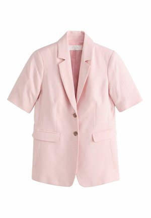 Žena má oblečený svetloružový krátky sako s krátkym rukávom a zodpovedajúce nohavice, stojí v interiéri chrbtom, cez okno sú viditeľné zelené stromy.