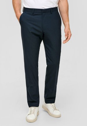 Navyblaue maßgeschneiderte Hose aus strukturiertem Stoff, schlanke Passform, mit Seitentaschen und einem glatten Bund. Kombiniert mit weißen Sneakern.