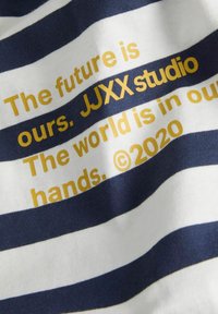 White and navy striped fabric displays golden text: "The future is ours. JJXX studio. The world is in our hands. ©2020."