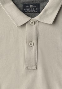 Světle šedý polo tričko s texturovanou tkaninou, tříknoflíkovou légou a límečkem. Obsahuje štítek s nápisem "Street One Men."