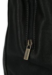 Zwart lederen materiaal met een close-up van een rits. De rits heeft een metalen trekker en een merketiket van "COWBOYSBAG."