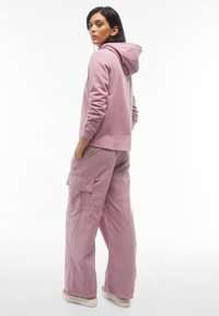 Felpa rosa in cotone con cappuccio e maniche lunghe, abbinata a pantaloni cargo larghi coordinati con tasche laterali e una vestibilità comoda.