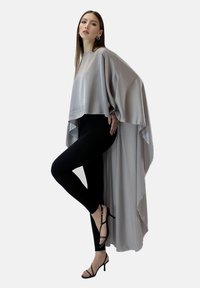 Hellgraues asymmetrisches Top aus Satin, mit weiten Ärmeln und fließendem Design, kombiniert mit schwarzen Leggings und schwarzen Sandalen mit Riemchen.