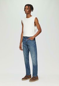 Witte mouwloze top, blauwe rechte jeans en bruine sneakers met streepaccenten. Soepele textuur, casual pasvorm en klassieke denim stijl.