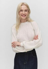 Vaahto beesi ribbed neule, jossa on tilavat hihat, pyöreä pääntie ja teksturoitu kangas, yhdistettynä tummiin farkkuhameeseen. Yksinkertainen tausta.