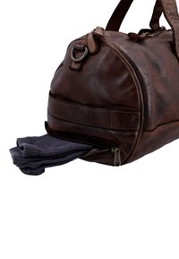 Brown leather duffel bag with side zipper pocket open, showing a pair of dark gray folded socks partially inside.