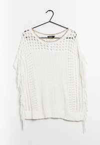 Pull en tricot blanc avec un design à mailles ouvertes. Présente des accents à franges sur les côtés et un col orné de chaînes. Suspendu à un crochet noir.