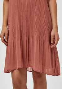 Krátké šatky barvy rzi s plisovanou strukturou, s volným lemem a krátkými rukávy, vyrobené z lehkého materiálu.