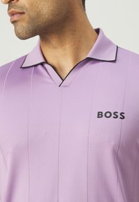 Šviesiai violetinė polo marškinėliai su juodu apvadu, su vertikaliomis juostelėmis ir išskirtiniu "BOSS" logotipu kairėje krūtinės pusėje.