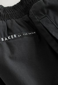 Melni auduma šorti ar elastīgu jostasvietu. Jostasvietā ir neliela balta logo uzraksts "BAKER by TED BAKER". Gluda tekstūra.