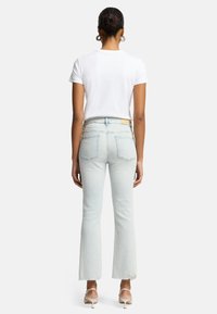 Jeans svasati azzurri chiari con orlo grezzo, caratterizzati da un alto punto vita, design a cinque tasche e un etichetta in pelle sul retro, indossati con una maglietta bianca.