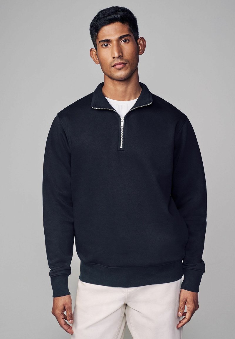 Zwarte rits-sweater van zacht materiaal, met een hoge kraag, lange mouwen en een aansluitende tailleband. Eenvoudig, strak ontwerp.