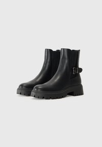 Sorte skinnankelsko med elastiske sidestykker, spenne detalj og tykke plattformsåler med mønster.