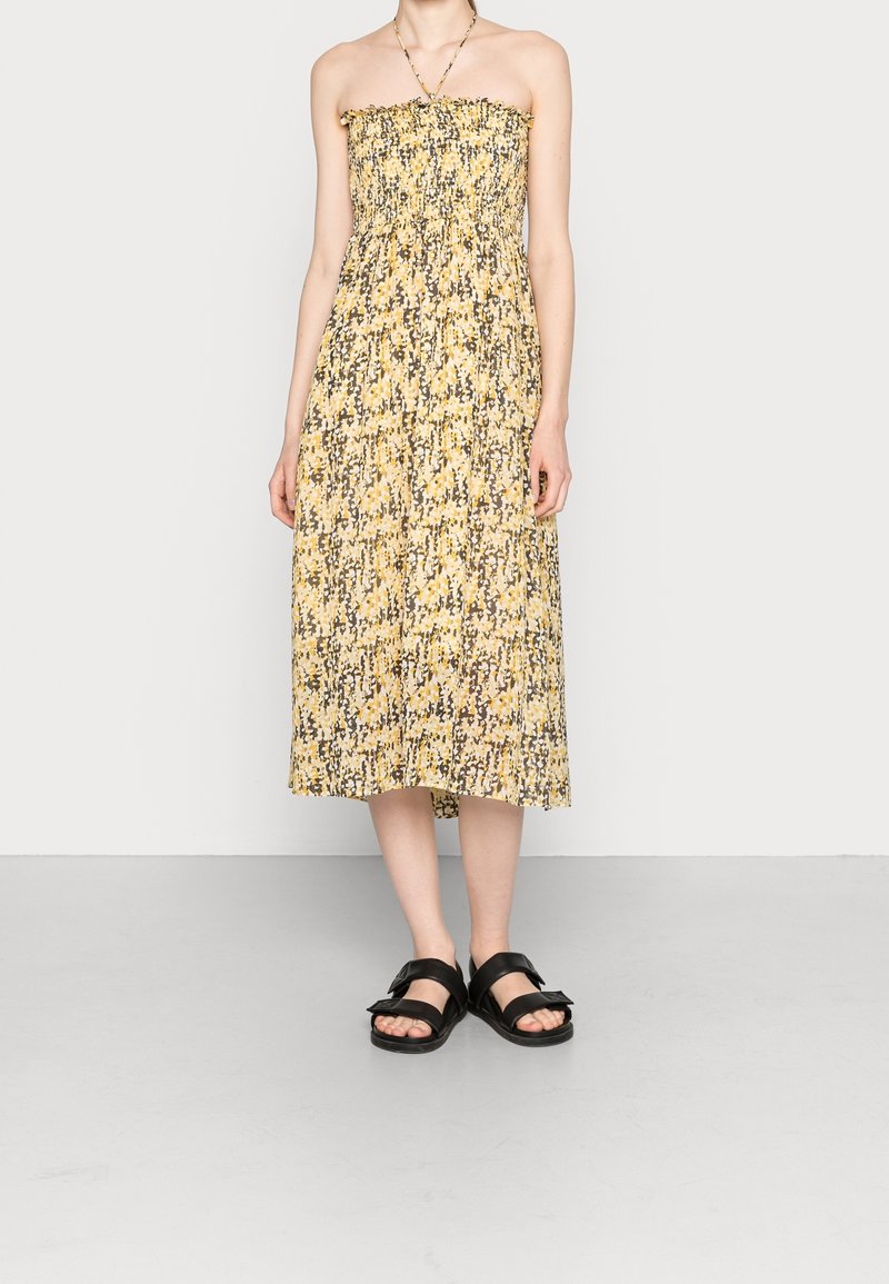 Bezramínkové sluneční šaty do půli kolen s abstraktním vzorem v žluté a šedé barvě. Mají smocked vršek a splývavou sukni. V kombinaci s černými sandály.