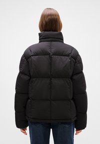 Μαύρο φουσκωτό μπουφάν με ψηλό γιακά, που διαθέτει ραφτό σχέδιο, μαξιλαρωμένα τμήματα και λείο, γυαλιστερό ύφασμα. Υφή.