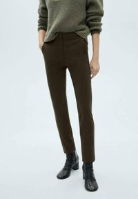 Pantaloni marroni su misura realizzati in un tessuto texture, caratterizzati da una vestibilità slim e vita media, abbinati a stivali neri alla caviglia.