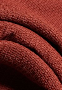 Zbliżenie na złożoną tkaninę z rdzawego, włóknistego materiału o teksturowanym, prążkowanym wzorze.