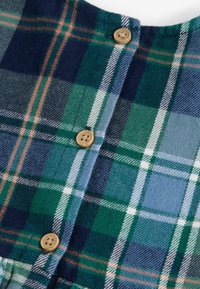 Fleece-skjorta med ett rutmönster i grönt, blått och vitt. Har träknappar och en rundad halsringning. Mjuk textur, medelviktigt tyg.