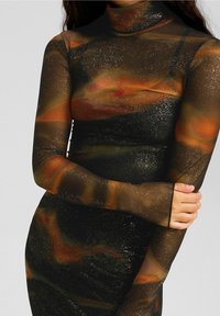 Svart nätklänning med långa ärmar, med ett abstrakt mönster i orange och guld med glittrande detaljer. Hög halsringning, figurnära silhuett.