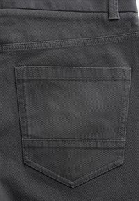 Gros plan d'une poche en tissu gris foncé cousue à l'arrière d'un pantalon avec une boucle de ceinture visible au-dessus.