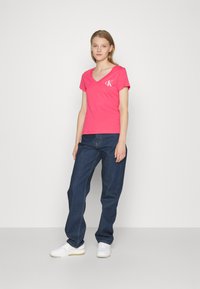 Camiseta de algodón rosa con escote en V y mangas cortas, combinada con jeans oscuros de corte holgado y zapatillas blancas.